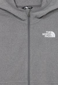 Pelēka zip-up vilnas jaka ar kapuci, uz kuras kreisajā krūtī ir izšūts balts The North Face logo.