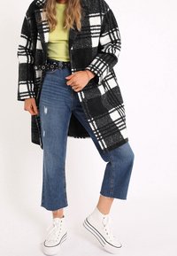 Cappotto grande a scacchi in bianco e nero, top verde, denim strappato e sneaker alte bianche. Presenta una vita cintrata e jeans a taglio dritto.