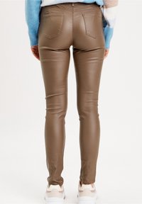Braune, synthetische Leder-Skinny-Jeans mit Gesäßtaschen, die eine glatte Textur und eine figurbetonte Passform aufweisen, kombiniert mit weißen Sportschuhen.