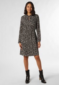 Zwarte en crèmekleurige jurk met patroon, lange mouwen, cinched taille, keyhole halslijn, gecombineerd met zwarte enkellaarsjes. Gladde stofstructuur.
