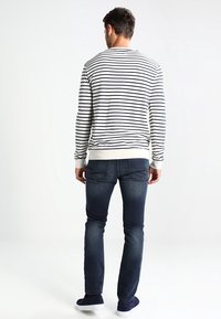 Pull pour homme à rayures crème et marine, avec un col rond et des poignets côtelés, associé à un jean skinny bleu foncé et des baskets bleu marine.