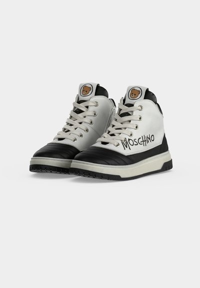 Paire de baskets montantes blanches et noires avec lacets, logo ourson sur la languette et "Moschino" écrit sur le côté.