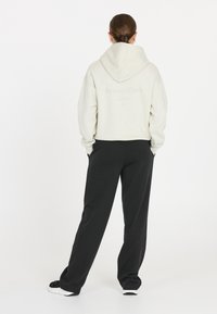 Ljusgrå huvtröja med texten "Sports Club" på ryggen, parat med lösa svarta sweatpants och svarta sneakers, sett bakifrån.