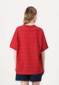 T-shirt vermelho de manga curta com um padrão circular em toda a peça, decote redondo, corte descontraído e a bainha a extender-se ligeiramente abaixo da cintura.