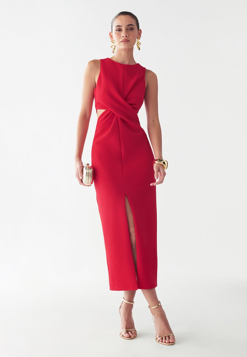 Red, sleeveless midi dress with a twist front and side cutouts, featuring a thigh-high slit. Smooth texture, complemented by metallic accessories.