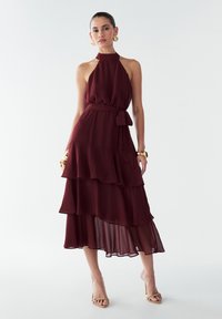 Bordo halterneck haljina s višeslojnim chiffon dizajnom, stegnutim pojasom i lepršavim rubom. Glatka textura i suptilni sjaj.