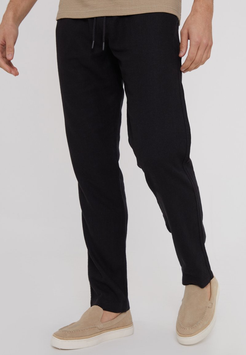 Pantalones azul oscuro de corte relajado, fabricados en un tejido suave. Cuentan con una cinturilla elástica con cordón, bolsillos laterales y detalles de costura sutiles.