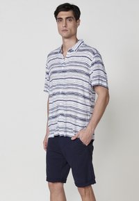 Krátky rukáv, košeľa na gombíky s námorníckymi a bielymi horizontálnymi pruhmi. Vyrobená z ľahkého materiálu, s golierom a vo voľnom strihu.