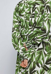 Langärmliges Kleid mit Blattmuster in grün und weiß, ausgestattet mit gerafften Manschetten mit elastischen Details und einer lockeren Passform.