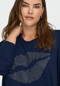 Granatowa bluzka z długim rękawem, wykonana z miękkiego materiału, z nadrukiem ust z srebrnych cyrkonii z przodu i okrągłym dekoltem.