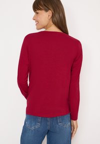 Langærmet, bordeaux top lavet af blødt, let stof, der har en afslappet pasform og rund udskæring. Kombineret med blå denim jeans.