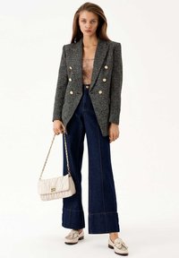 Blazer doppiopetto grigio in tweed con bottoni dorati, abbinato a pantaloni flare in denim a vita alta e una borsa trapuntata color crema. Mocassini beige.