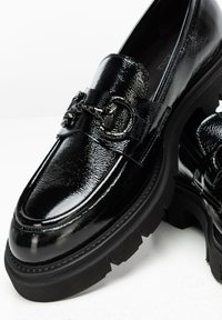 Mocassini in vernice nera con suola spessa, dotati di una catena decorativa sulla parte anteriore e design della punta arrotondata.