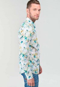 Witte langemouwen shirt met een bloemenpatroon van blauwe en gele botanische ontwerpen, gecombineerd met blauwe jeans.