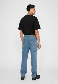 Black crew neck t-shirt paired with light blue cargo jeans featuring multiple pockets and a leather patch on the back waistband. Black shoes.