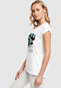 Weißes Baumwoll-T-Shirt mit umgeschlagenen Ärmeln, das einen grafischen Druck in Schwarz und Türkis zeigt, mit Figuren und Text auf der Vorderseite.
