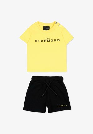 Chemise jaune à manches courtes avec le texte « John Richmond » et short noir à cordon de serrage avec un logo assorti sur la jambe gauche.
