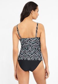 Zwarte zwemtop met een geometrisch patroon in wit en teal, voorzien van verstelbare bandjes en een effen zwarte onderkant. Glad, textuurmateriaal.