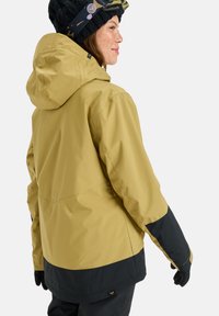 Gelbe wasserdichte Jacke mit einem schwarzen unteren Teil, Kapuze und verstellbaren Manschetten. Das Material wirkt glatt mit einer matten Oberflächenbeschaffenheit.