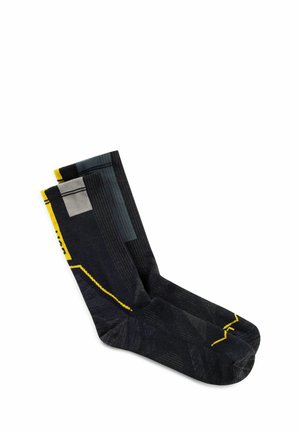 Calcetines negros de media caña con detalles geométricos en amarillo y gris, doblados uno al lado del otro sobre un fondo blanco.
