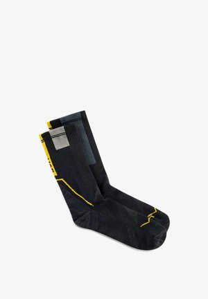 Calcetines negros de media caña con detalles geométricos en amarillo y gris, doblados uno al lado del otro sobre un fondo blanco.