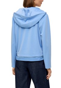 Lichtblauwe hoodie met een trekkoord in de capuchon, gemaakt van zachte stof. Heeft een comfortabele pasvorm en ribgebreide manchetten, gecombineerd met donkere spijkerbroeken.