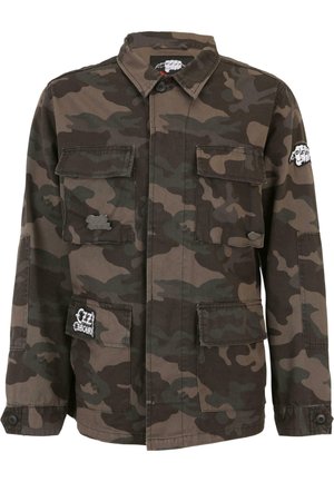 Camo-jack in katoenmix, met twee borstzakken, knoopsluiting en geborduurde accenten. De dominante kleuren zijn donkergroen en bruin.