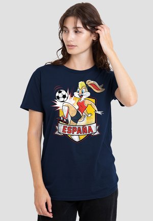 Frau trägt ein marineblaues T-Shirt mit einem Cartoon-Hasen, der Fußball spielt, und dem Wort España auf einem rot-gelben Schild-Hintergrund.
