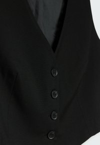 Gilet nero con design a scollo a V, caratterizzato da cinque bottoni neri e tessuto liscio. Pannelli aggiuntivi conferiscono struttura all'indumento.