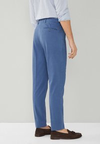 Blauwe chino's met een gladde textuur, voorzien van een achterzak met knoopsluiting, gestyled met een licht geruit overhemd en donkere loafers.