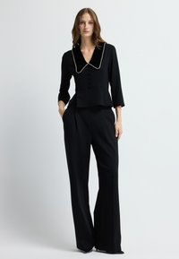 Černý peplum top s velkým límcem, složitými detaily knoflíků a černými širokými kalhotami, vše vyrobené z hladkého materiálu.