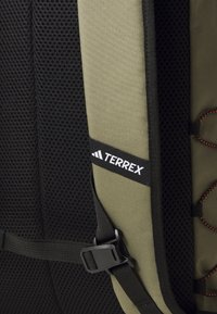 Nahrbtnik z zeleno tkanino in črnimi mrežastimi paneli, ki ima oranžne akcentne detajle, nastavljive naramnice in bel logotip "Terrex".