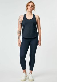 Tumesinine tank top, mis on valmistatud pehmest kangast ja millel on lõdvendatud istuvus, koos napide tumesiniste retuuside ja valgete spordijalatsitega, et saavutada sportlik välimus.