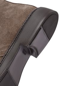 Suela de zapato de ante marrón con áreas del talón y de los dedos de goma negra texturizada, costuras visibles a lo largo del borde.