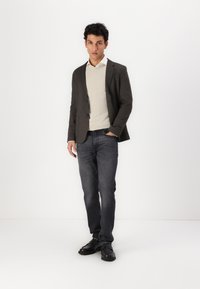 Donkergrijze blazer over een crèmekleurige trui, gecombineerd met donkere jeans en zwarte schoenen. De materialen lijken glad met een aansluitend ontwerp.