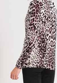 Osoba w długim rękawie sweterze w zwierzęcy wzór z czarnymi i brązowymi plamami, zestawionym z czarnymi spodniami, pokazana z boku i z tyłu.