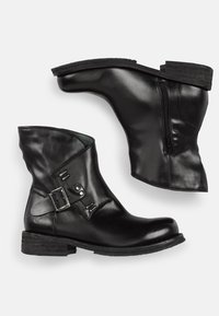 Botas de tobillo de cuero negro con un corte curvado, cremallera lateral y detalle de hebilla plateada. Suela texturada y acabado suave.