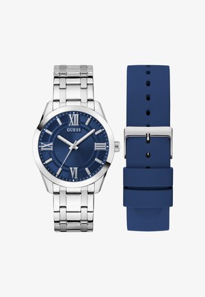Montre-bracelet en métal argenté avec cadran bleu, chiffres romains et aiguilles argentées, à côté d'un bracelet de remplacement en silicone bleu avec boucle métallique.