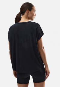 Top negro de manga corta con un corte relajado y dobladillo redondeado, que presenta un sutil detalle de costura en la parte posterior y una textura suave y lisa.