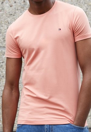 Lichtroze T-shirt met korte mouwen van zacht katoen, met een klein logo op de borst. Gecombineerd met blauwe spijkerbroek.