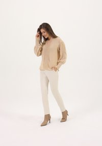 Pull en tricot beige avec des panneaux texturés, décolleté en V et manches volumineuses, associé à un pantalon écru et des bottines taupe.