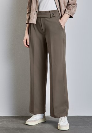 Pantaloni a gamba larga in un tessuto marrone tenue, con tasche laterali e chiusura a bottone. Abbinati a sneakers bianche per un contrasto.