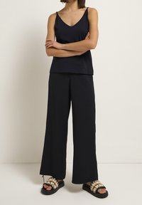 Top nero senza maniche, pantaloni neri larghi e sandali Chunky neri e crema. Tessuto morbido, design a V e silhouette ampia.