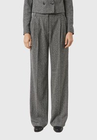 Czarno-białe spodnie o szerokich nogawkach w jodełkę, z wysokim stanem, plisami z przodu i luźnym krojem, zestawione z czarnymi butami.