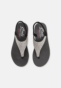 Svarte flip-flops med en teksturert såle og rhinestonesdekkede stropper. Har design med mellomrom mellom tærne og en myk yogaskum fotbed for komfort.