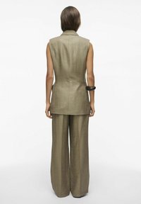 Chaleco sin mangas beige, con un cuello estructurado y una abertura en la parte trasera, combinado con pantalones de tiro alto de pierna amplia a juego.