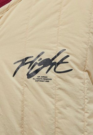 Chaqueta acolchada beige con un cuello de color burdeos. Logo negro "Flight" con detalles de marca impresos en el pecho. Acabado de tela texturizada.