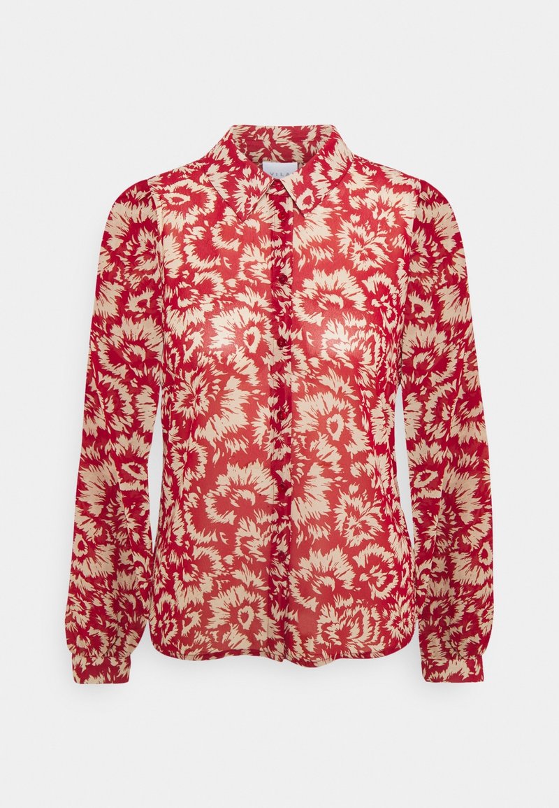 Röd blus med blommönster och genomskinlig textur, med krage och långa ärmar. Mönstret består av krämfärgade blommor på en röd bakgrund.