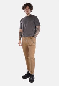 Camiseta gris combinada con pantalones caqui ajustados que presentan un detalle de cadena. Zapatillas deportivas negras completan el atuendo. Textura de tela suave.