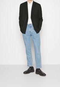 Schwarzes Blazer mit Reißverschlusstasche, weißes Hemd, hellblaue Jeans mit geradem Bein und schwarze Mokassins. Sauberes Design und taillierte Passform.